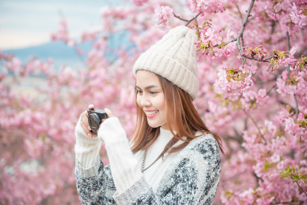 girl holding a camera with cherry blossom trees behind her
