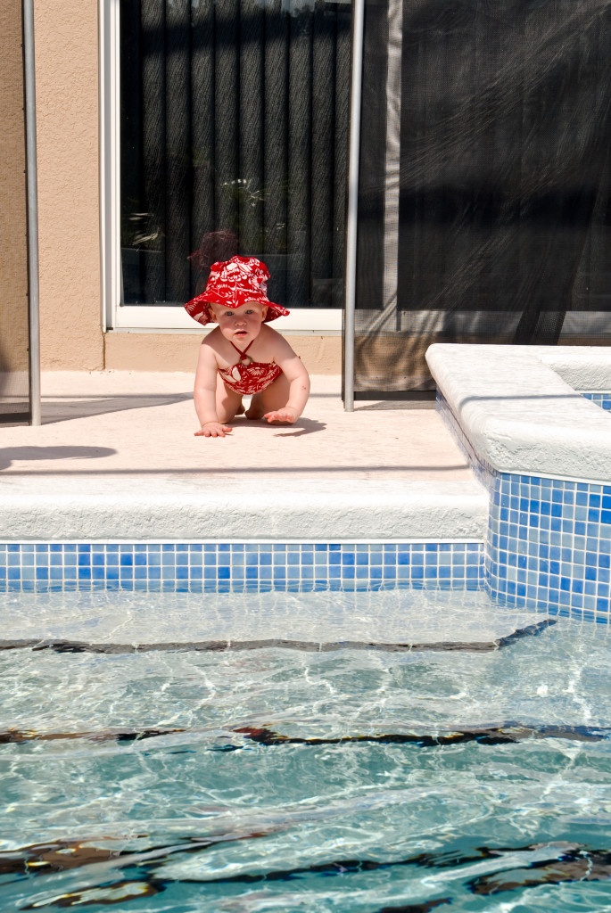 A young baby crawls through the opening of the safety fence left open. No adults appear to be near the child as she moves toward the swimming pool.