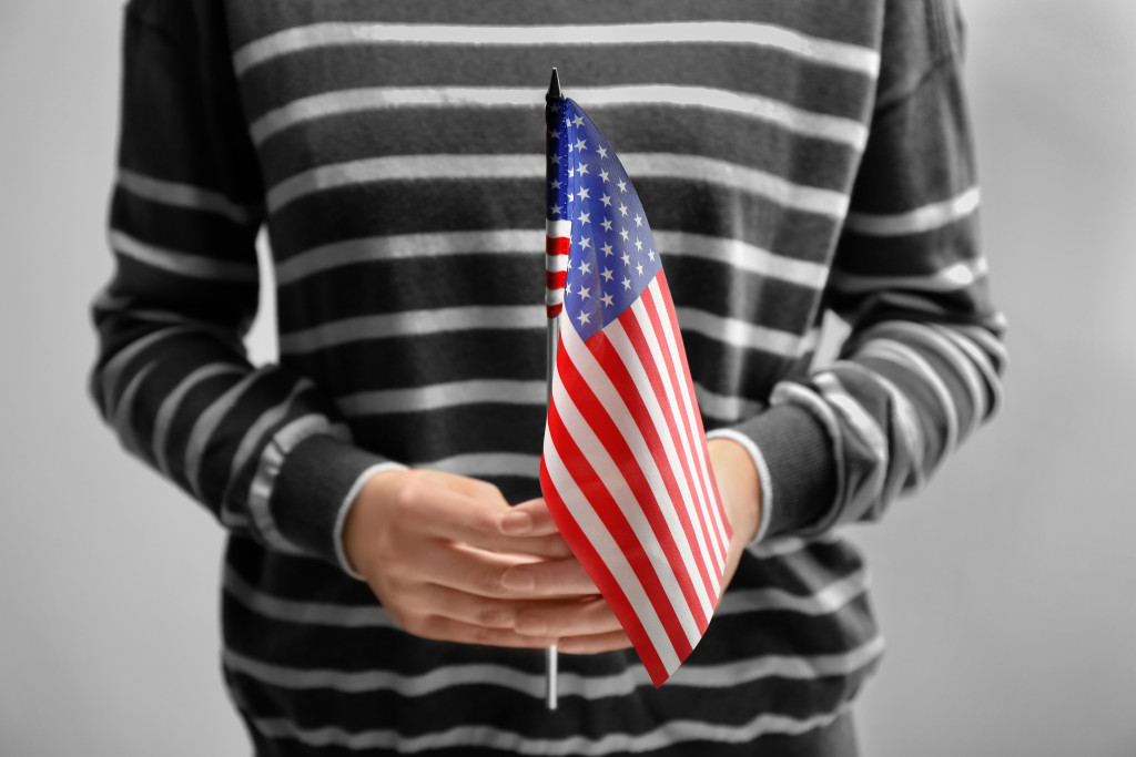 American woman holding an American flag while wearing a striped sweatshirt.