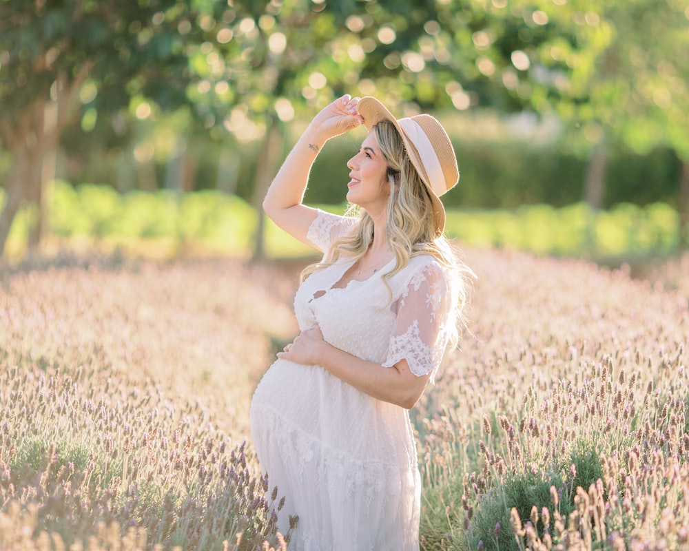 A Pregnant Woman in White Dress Wearing Sun Hat while Looking Afar