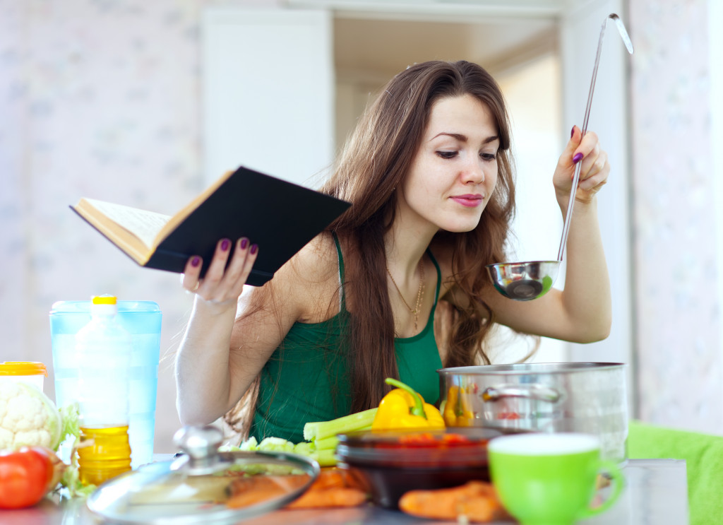 A woman cooking with a ladle and a cookbook in the kitchen