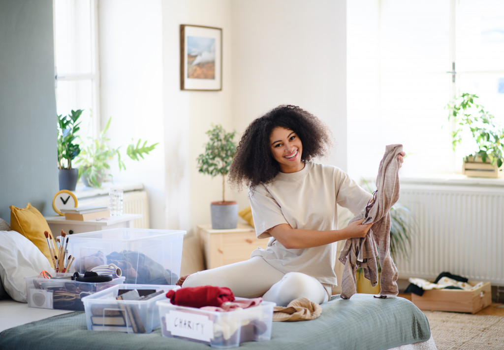 happy curly haired woman decluttering her room and sorting things in containers