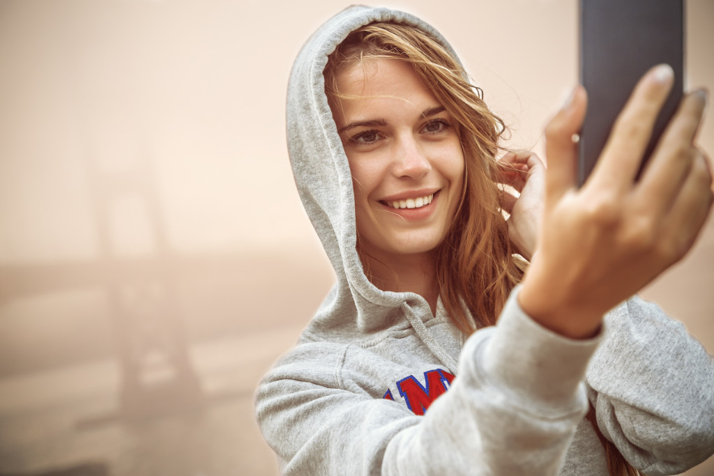 Young woman taking a selfie with a fog-covered bridge in the background.